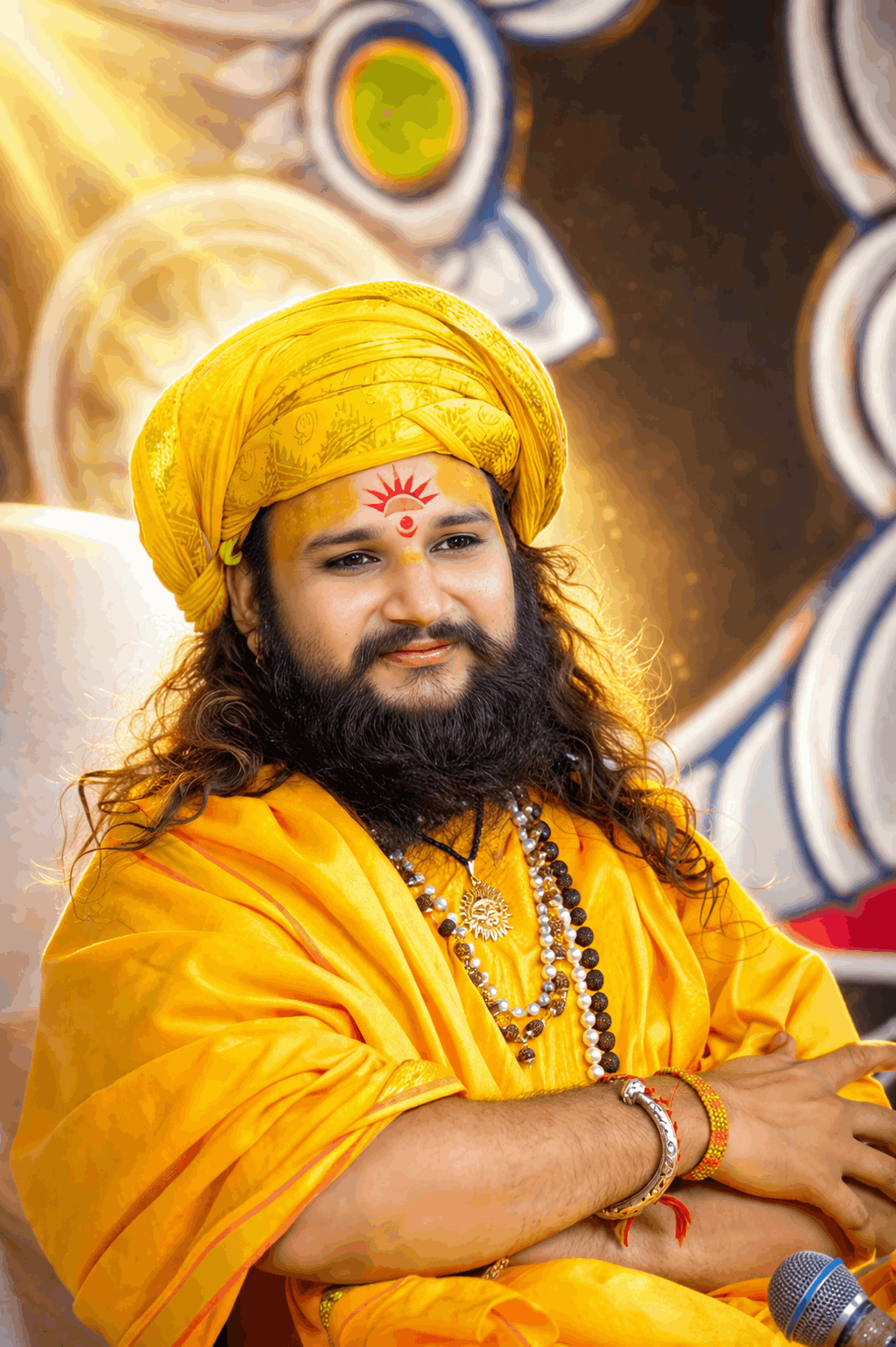 “Maharaj Ji speaking on stage during religious discourse with audience and devotional setup”